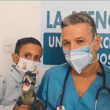 Un médico junto a un niño que sostiene un dinosaurio de juguete